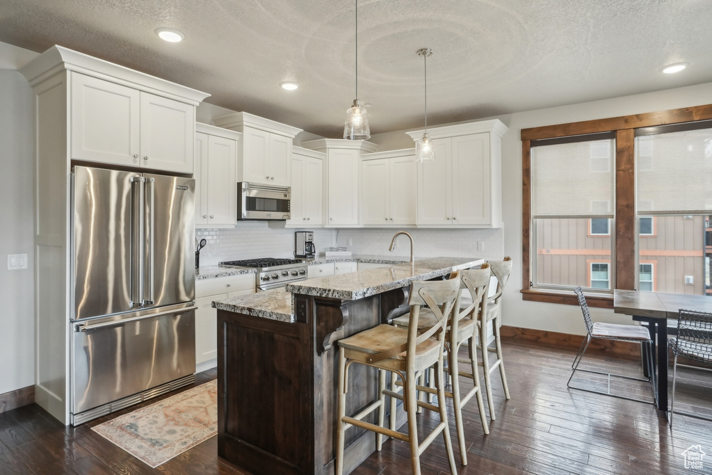Kitchen with dark wood-type flooring, an island with sink, tasteful backsplash, and appliances with stainless steel finishes