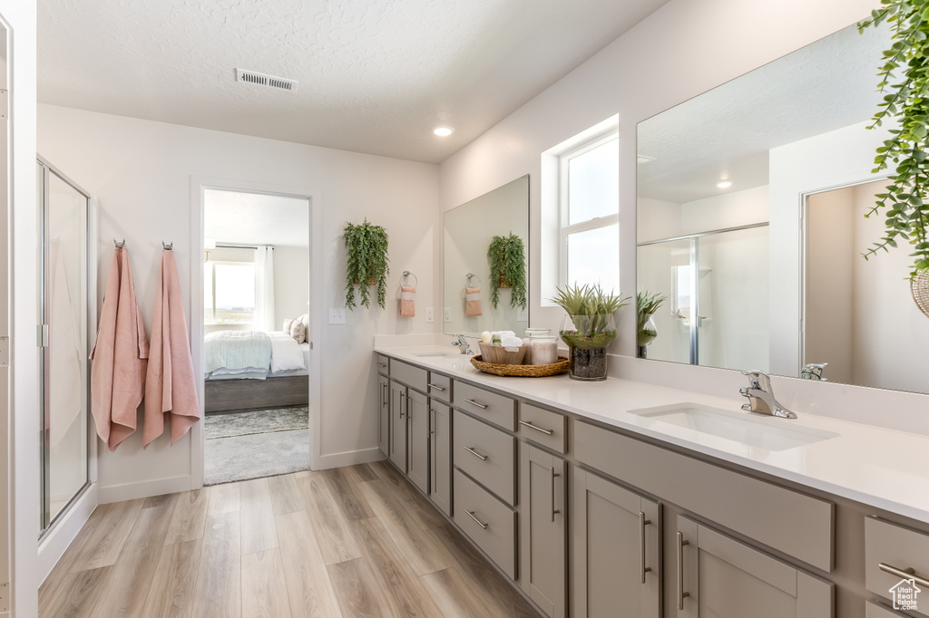 Ensuite bathroom with a shower stall, a sink, visible vents, double vanity, and wood finished floors
