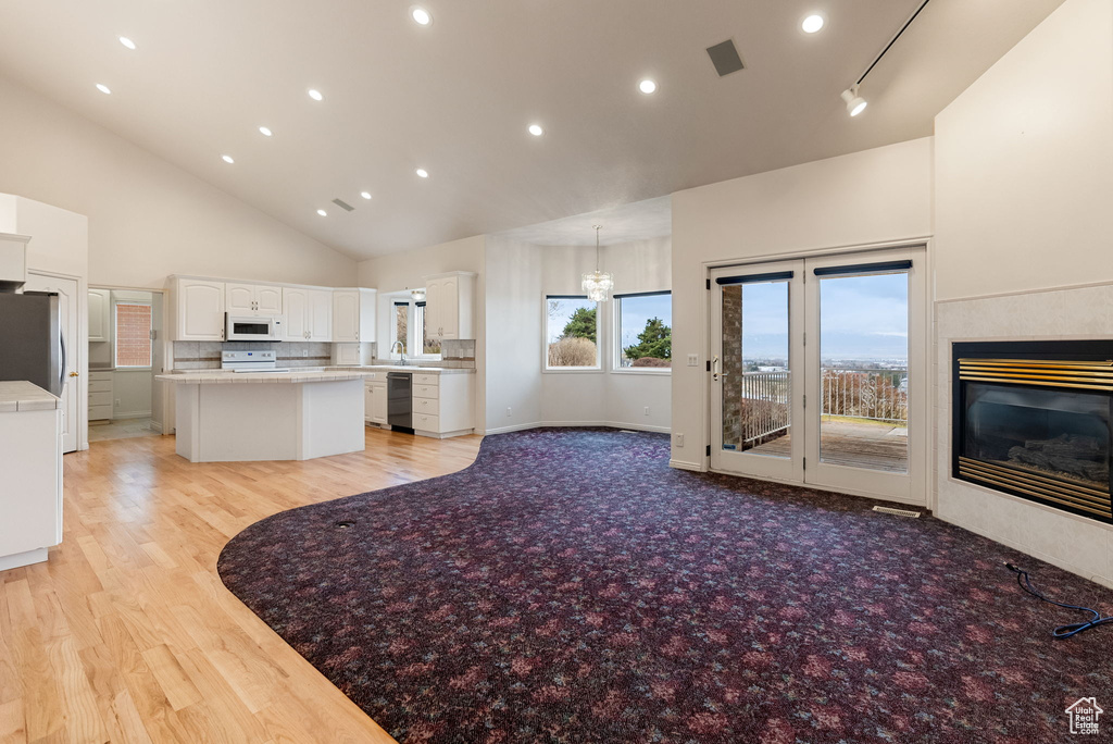Kitchen featuring high vaulted ceiling, white cabinets, white appliances, a kitchen island, and a glass covered fireplace