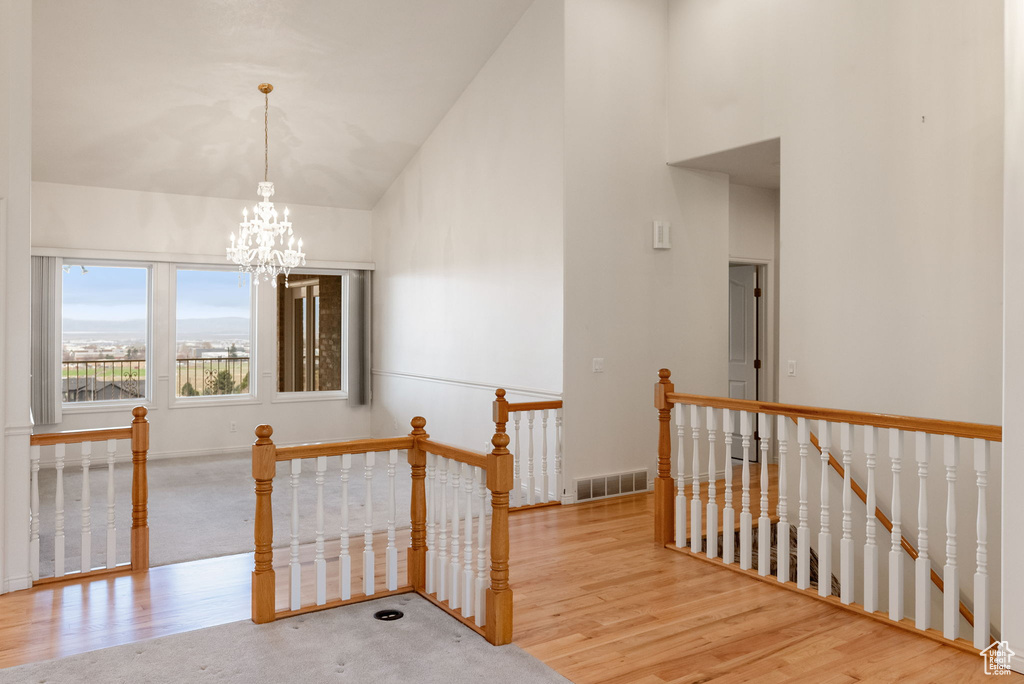 Corridor featuring high vaulted ceiling, an upstairs landing, a chandelier, wood finished floors, and visible vents