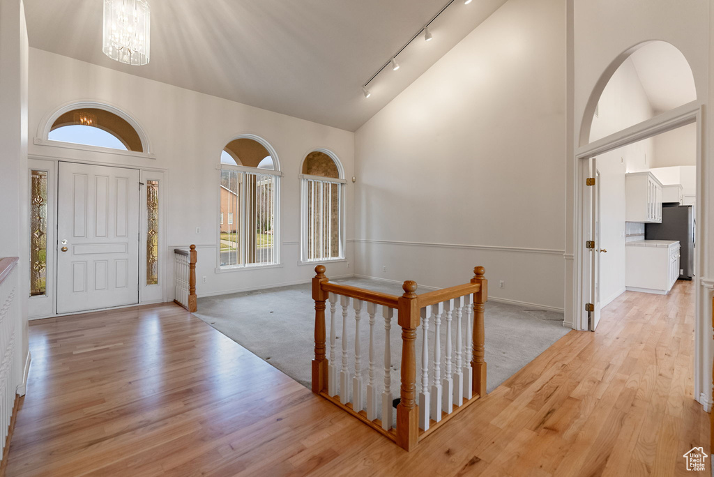 Foyer featuring high vaulted ceiling, light wood-style flooring, track lighting, and an inviting chandelier