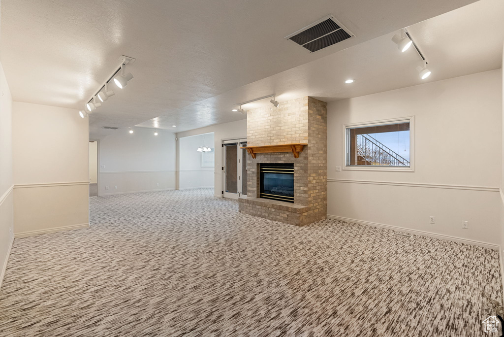 Unfurnished living room featuring a fireplace, visible vents, track lighting, and carpet