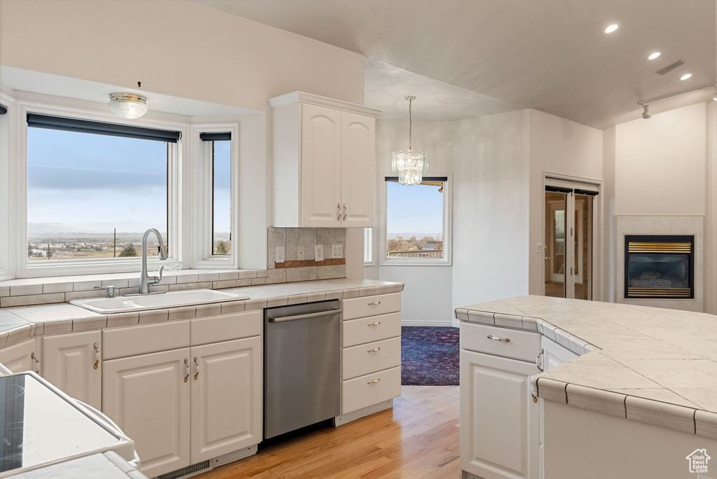 Kitchen with white cabinetry, stainless steel dishwasher, a sink, tile countertops, and light wood finished floors