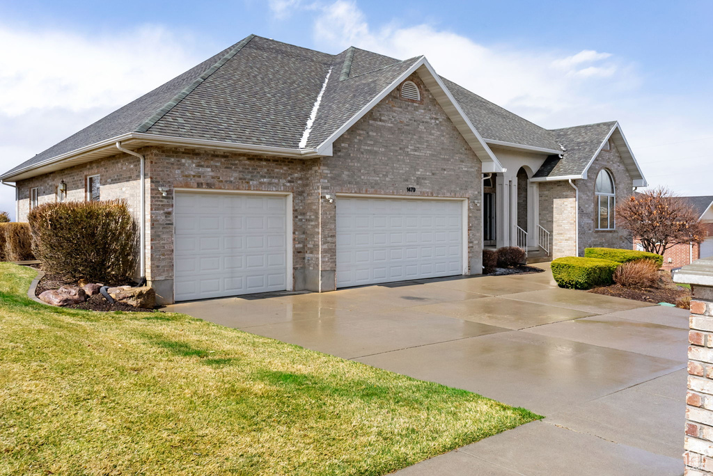 View of side of property with roof with shingles, an attached garage, driveway, brick siding, and a yard
