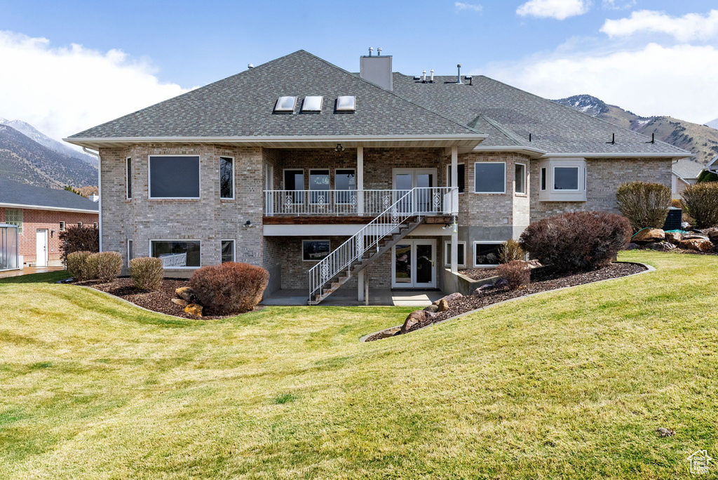 Back of house with stairs, brick siding, a shingled roof, a mountain view, and a yard