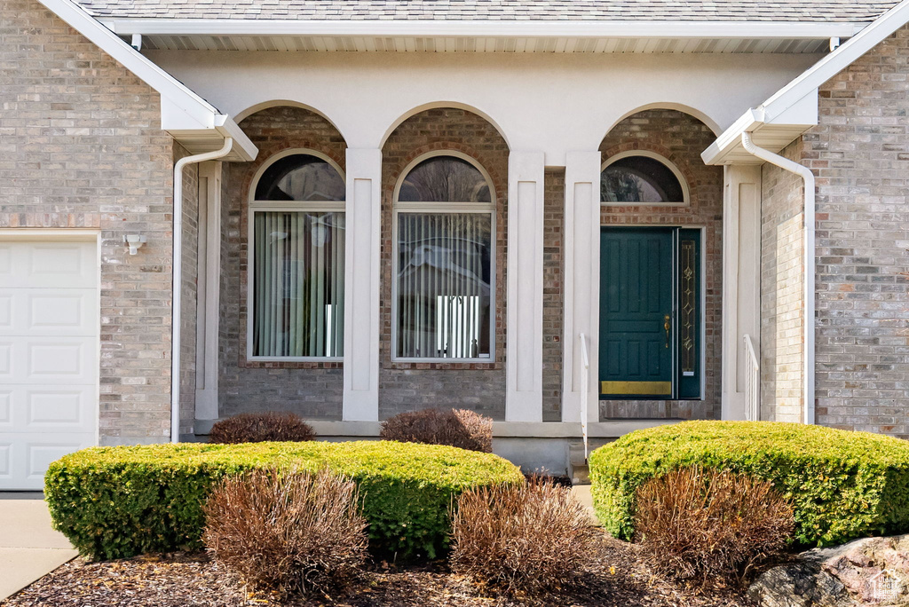 Entrance to property featuring a garage, brick siding, and roof with shingles