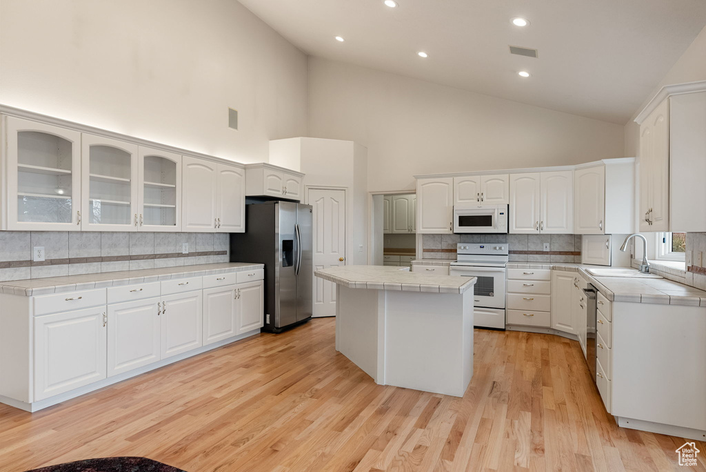 Kitchen with tile counters, a kitchen island, appliances with stainless steel finishes, glass insert cabinets, and a sink