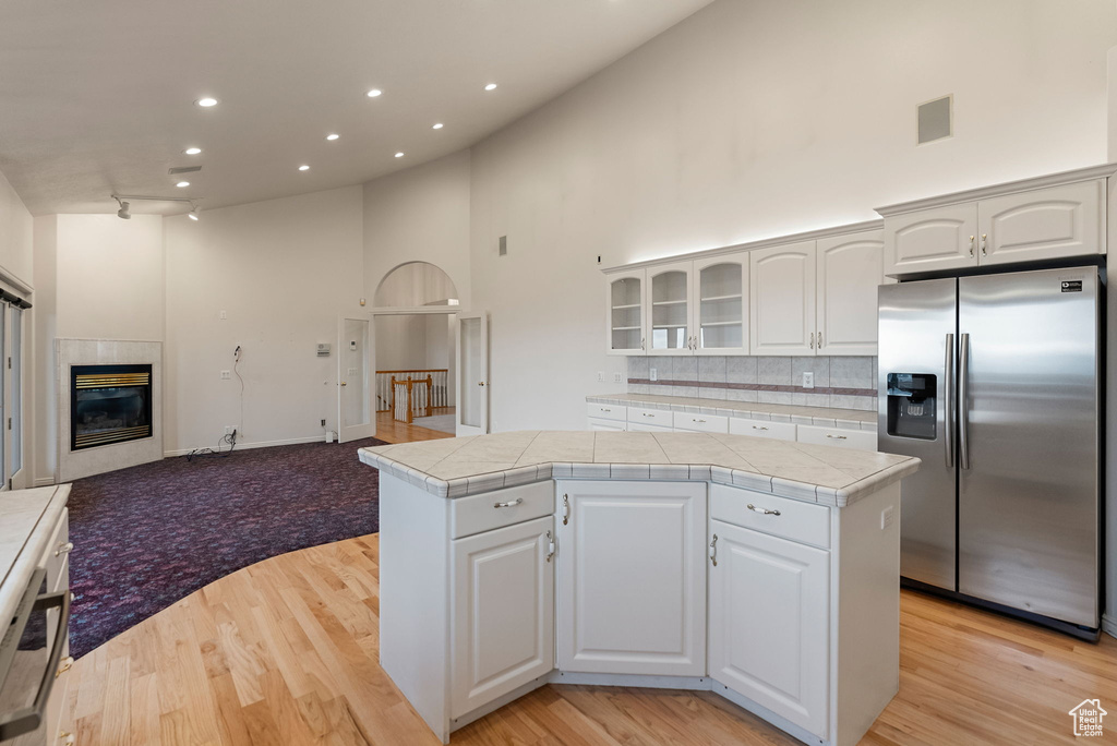Kitchen featuring high vaulted ceiling, glass insert cabinets, stainless steel refrigerator with ice dispenser, open floor plan, and a center island