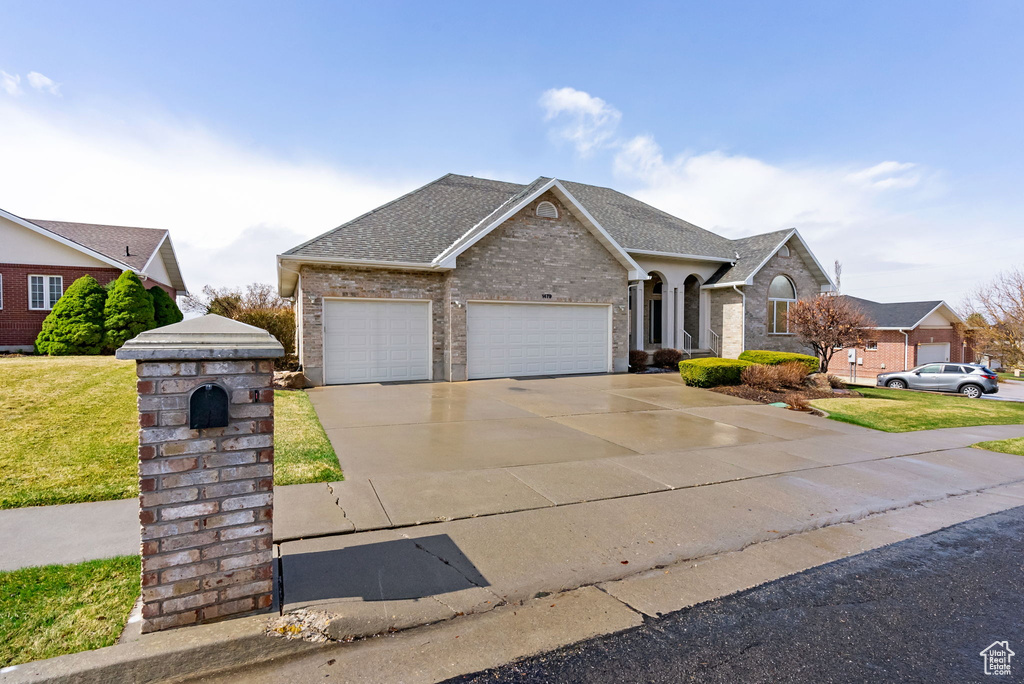 View of front of property featuring concrete driveway, roof with shingles, an attached garage, a front lawn, and brick siding