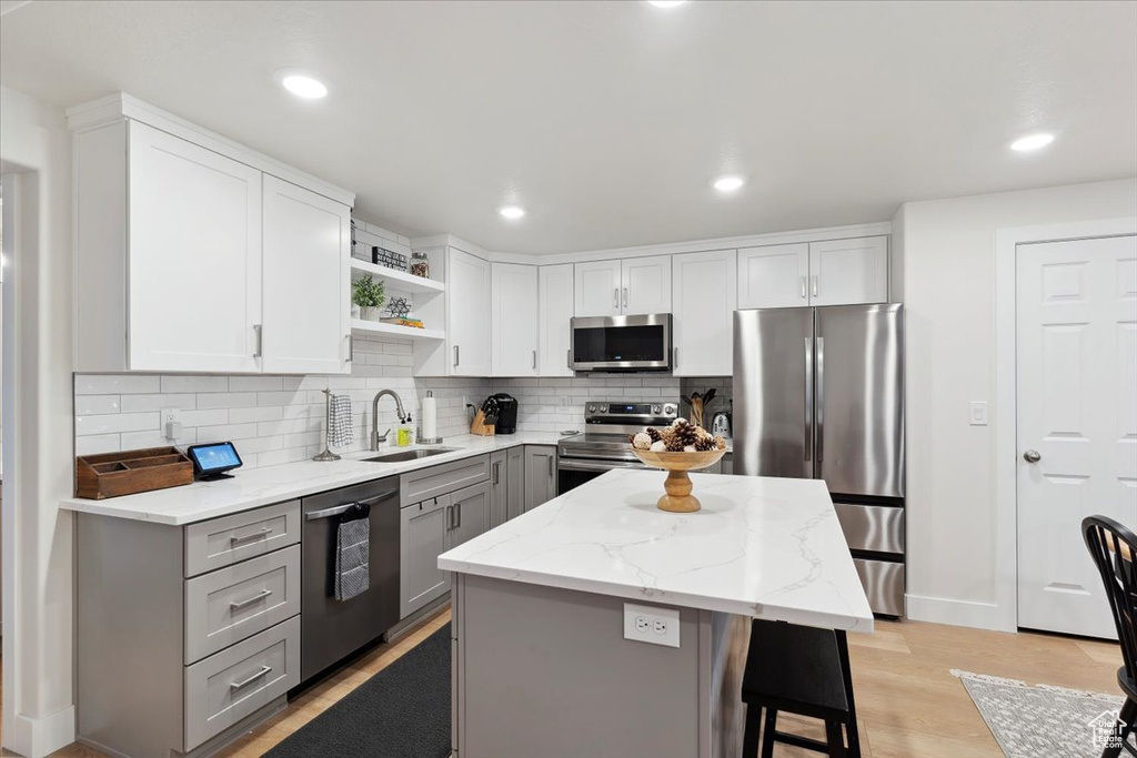 Kitchen with gray cabinets, decorative backsplash, appliances with stainless steel finishes, open shelves, and a sink