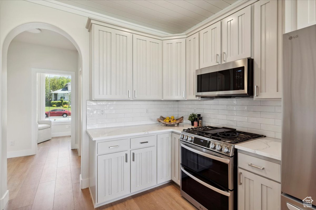 Kitchen with decorative backsplash, light stone countertops, light wood-style floors, arched walkways, and appliances with stainless steel finishes