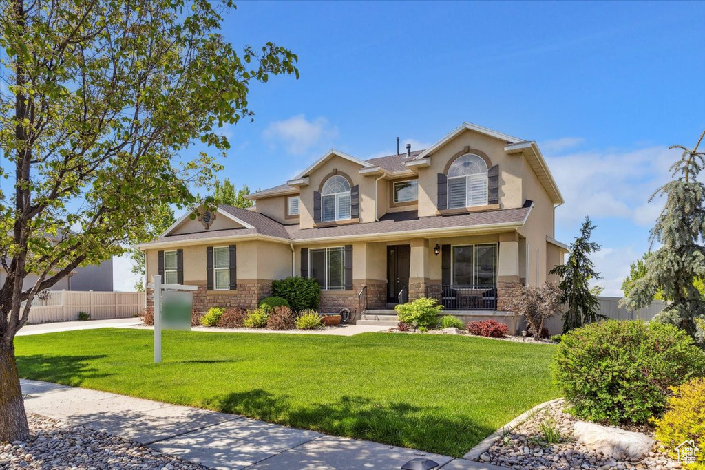 View of front of house with fence, stucco siding, a front lawn, and stone siding
