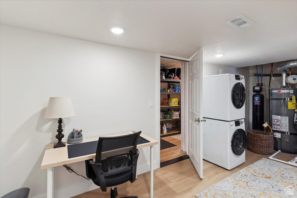 Laundry room with stacked washer / drying machine, laundry area, secured water heater, light wood-type flooring, and visible vents