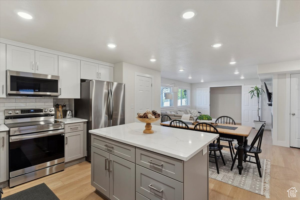 Kitchen featuring backsplash, stainless steel appliances, gray cabinetry, and light wood-style flooring