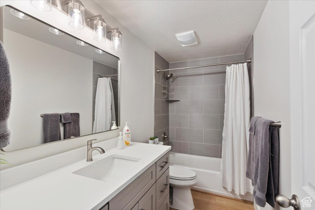 Bathroom featuring vanity, toilet, a textured ceiling, shower / bath combination with curtain, and wood finished floors
