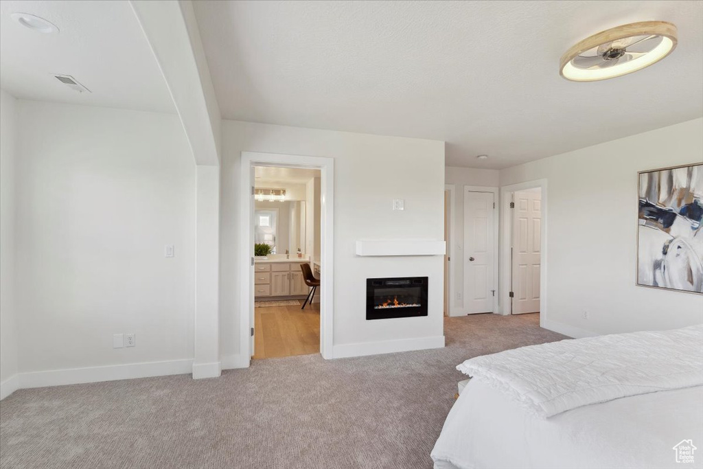 Bedroom featuring light carpet, ensuite bath, a glass covered fireplace, baseboards, and visible vents
