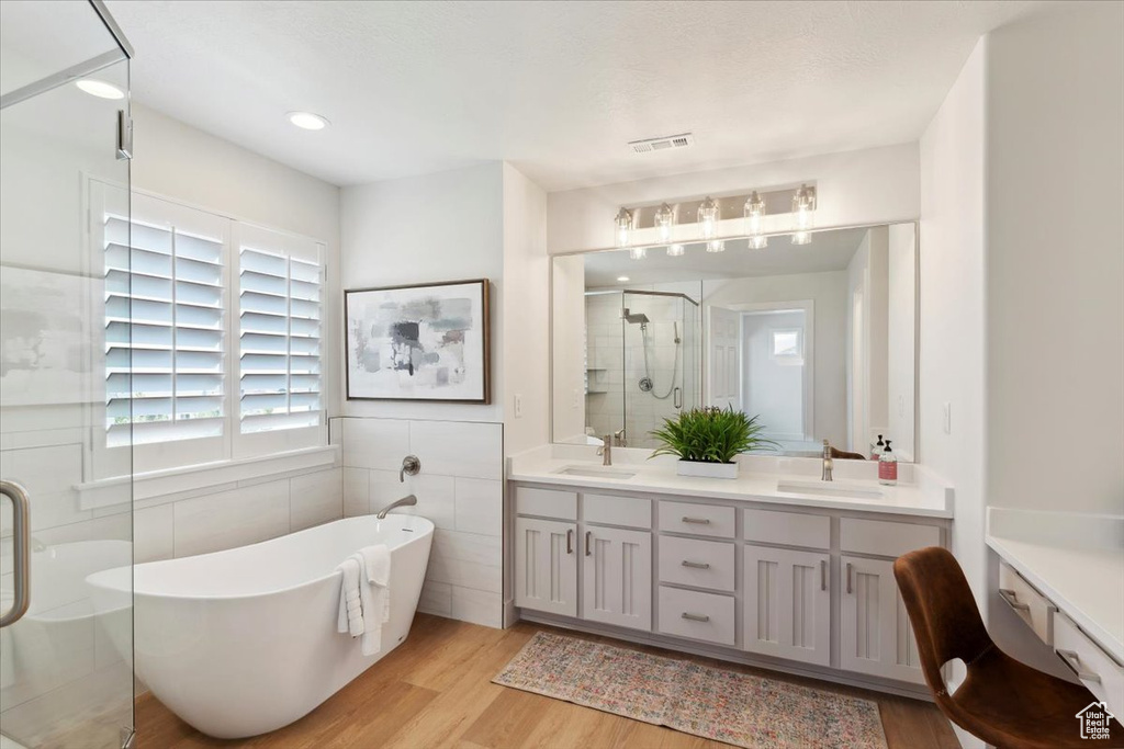 Bathroom with double vanity, visible vents, a shower stall, wood finished floors, and a sink