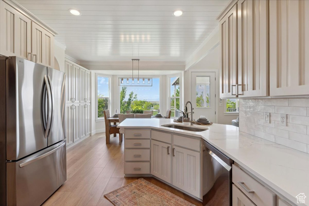 Kitchen featuring appliances with stainless steel finishes, a sink, light wood-style floors, a peninsula, and decorative backsplash