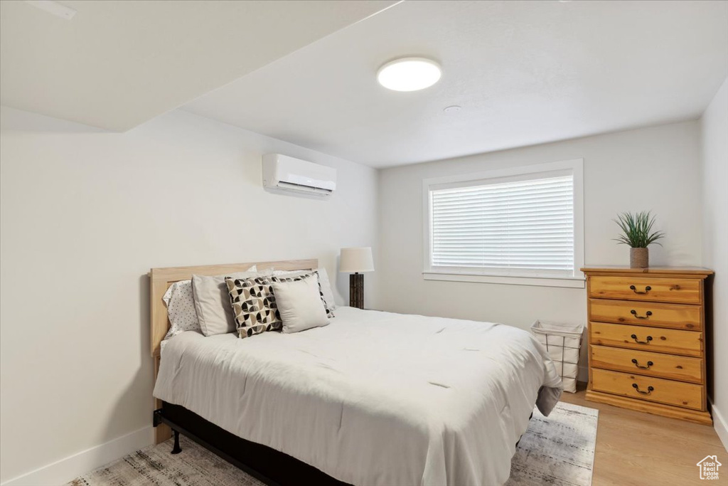Bedroom with light wood-style floors, baseboards, and a wall unit AC