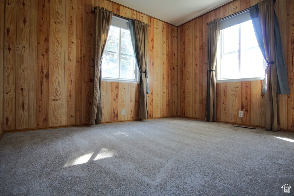 Unfurnished room featuring light colored carpet, wooden walls, and visible vents