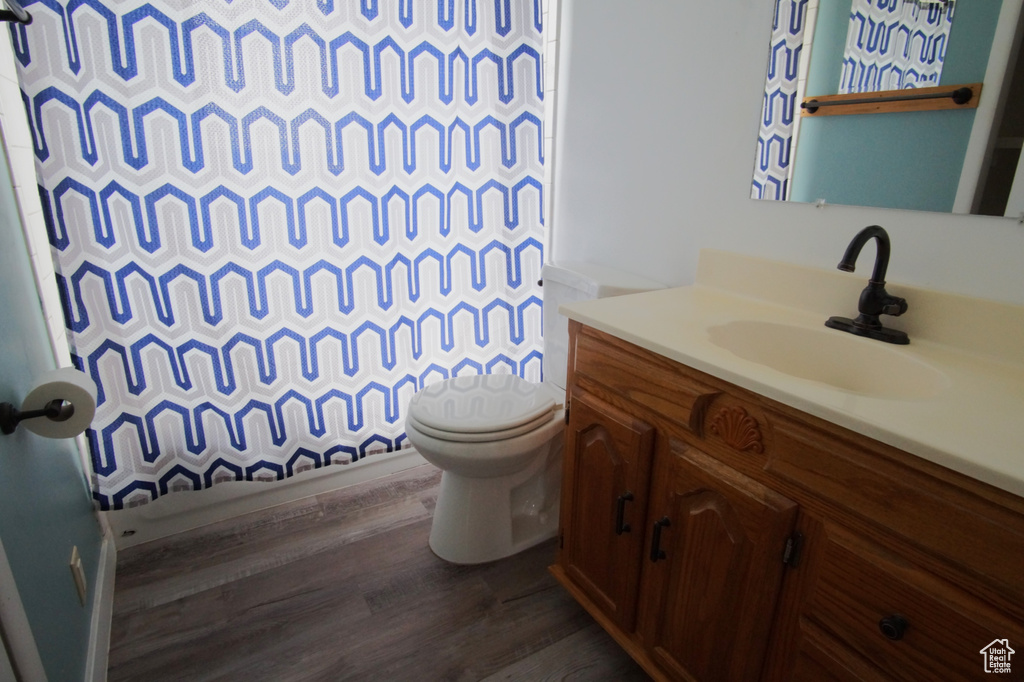 Bathroom with a shower with shower curtain, wood finished floors, toilet, and vanity