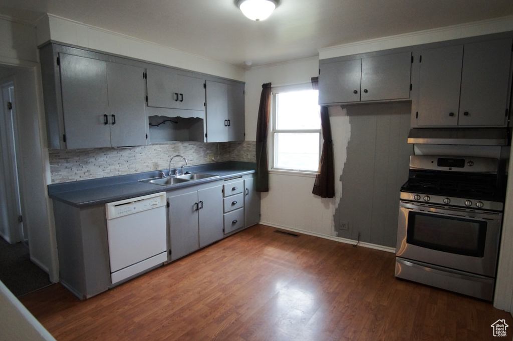 Kitchen featuring under cabinet range hood, stainless steel gas stove, a sink, dark wood-style floors, and white dishwasher