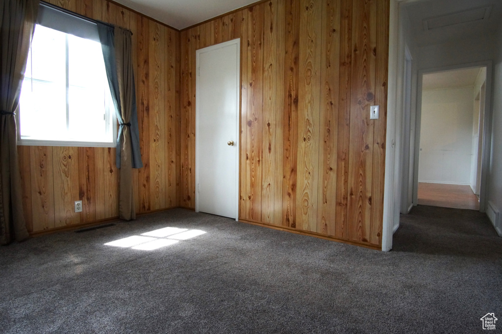 Carpeted empty room with visible vents and wood walls