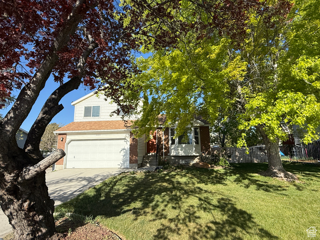 View of property hidden behind natural elements with fence, an attached garage, driveway, and a front lawn