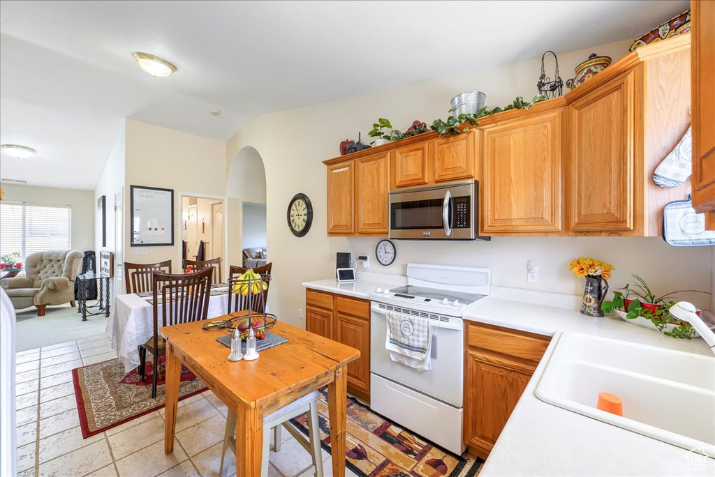 Kitchen featuring light countertops, stainless steel microwave, electric stove, a sink, and vaulted ceiling