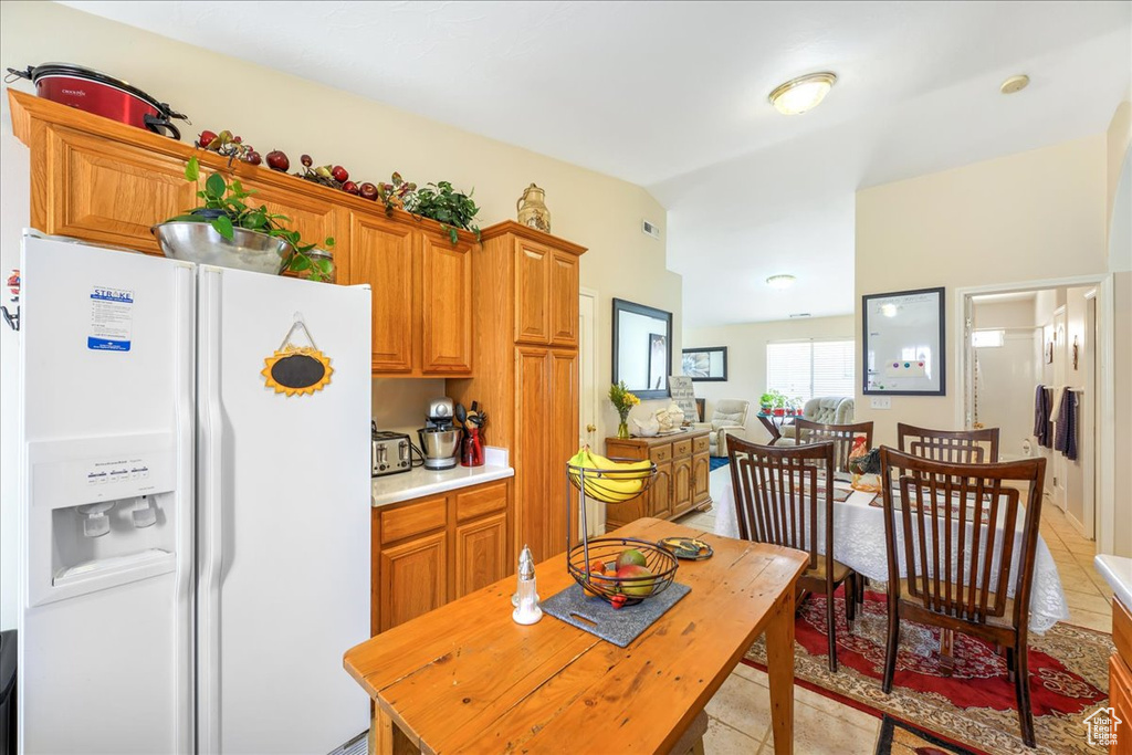 Kitchen with vaulted ceiling, light countertops, white refrigerator with ice dispenser, brown cabinets, and light tile patterned floors