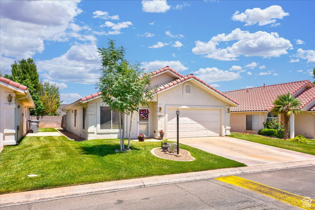 View of front of home with a tile roof, concrete driveway, stucco siding, an attached garage, and a front lawn