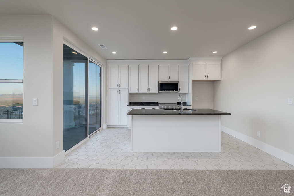 Kitchen with stainless steel microwave, a sink, white cabinetry, recessed lighting, and dark countertops