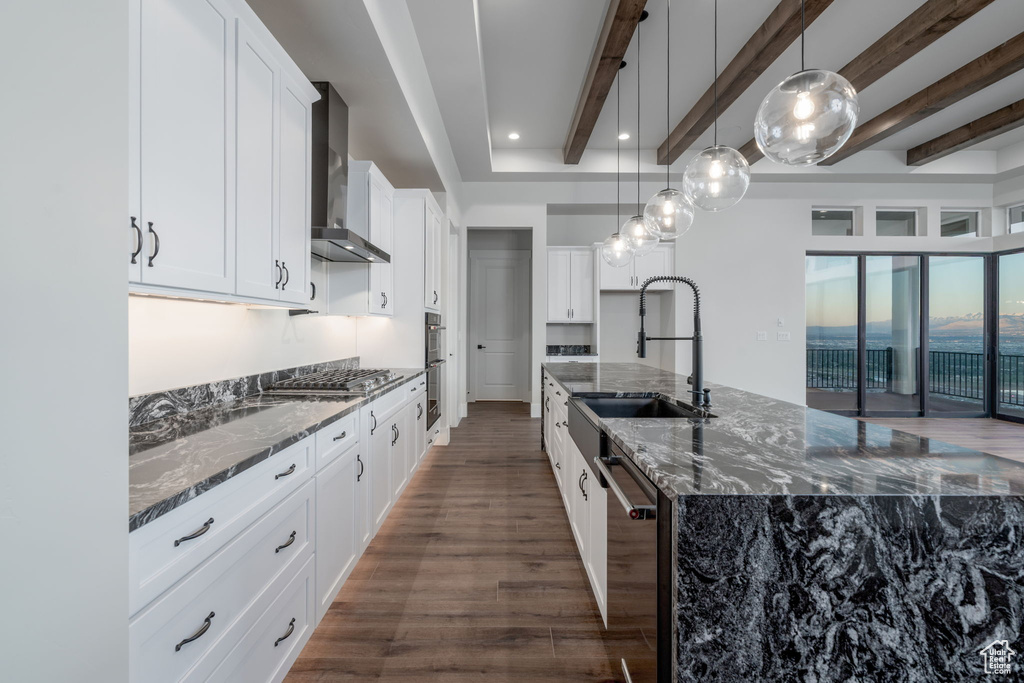Kitchen featuring wall chimney exhaust hood, dark wood-type flooring, stainless steel appliances, a sink, and beamed ceiling