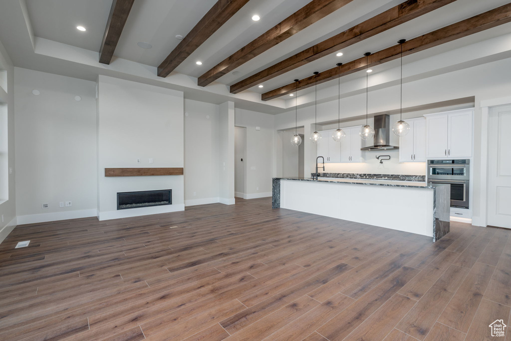 Unfurnished living room with beam ceiling, a glass covered fireplace, dark wood-type flooring, a sink, and baseboards