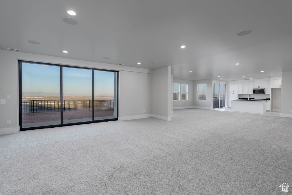 Unfurnished living room featuring baseboards, light colored carpet, and recessed lighting