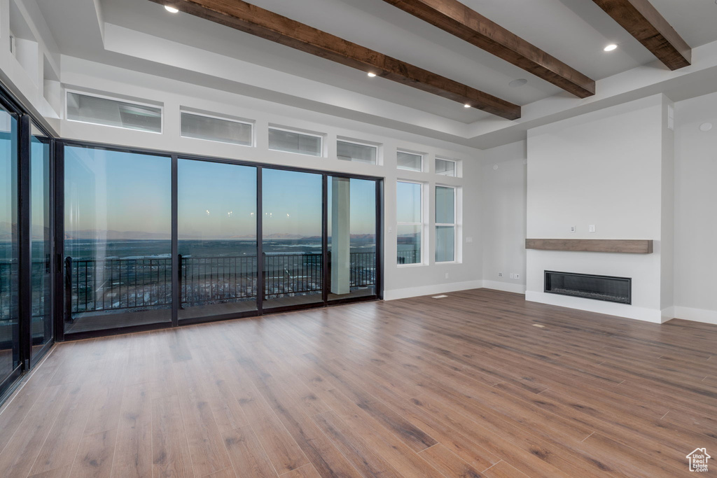 Unfurnished living room with beamed ceiling, a glass covered fireplace, baseboards, and wood finished floors