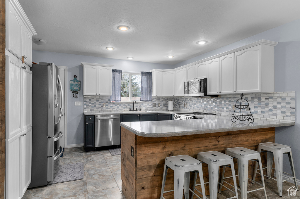 Kitchen featuring a breakfast bar, decorative backsplash, white cabinets, a peninsula, and appliances with stainless steel finishes