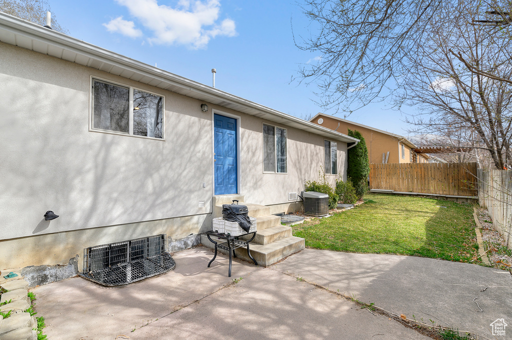 Back of property with a patio area, stucco siding, fence, central AC unit, and a lawn