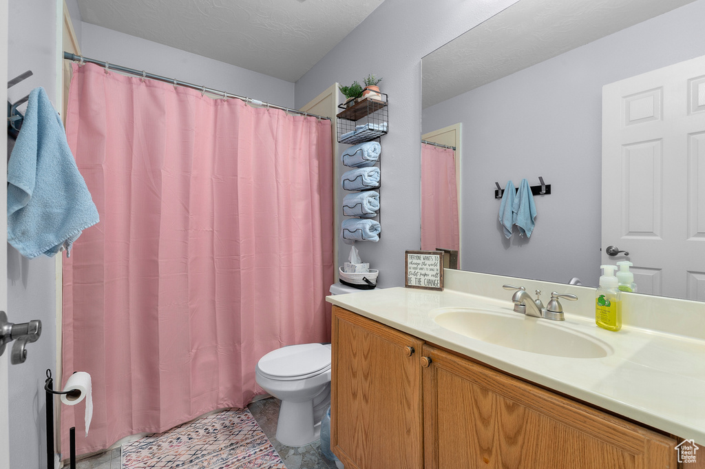 Bathroom featuring curtained shower, a textured ceiling, toilet, and vanity