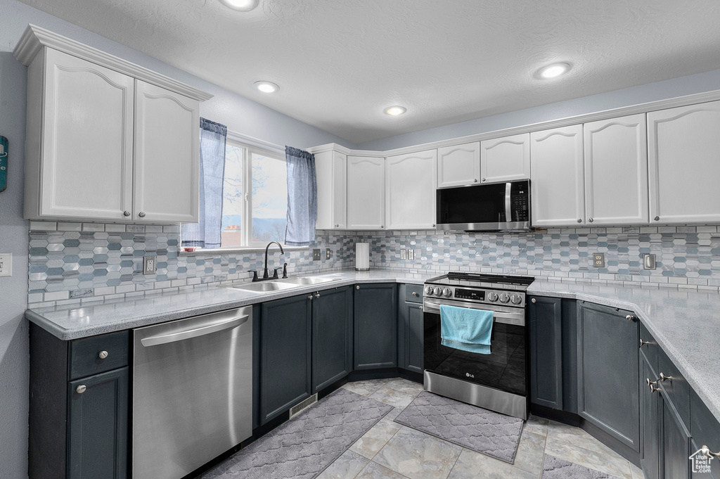 Kitchen featuring white cabinetry, light countertops, stainless steel appliances, backsplash, and a sink