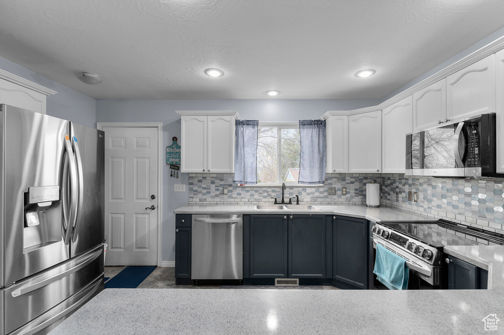 Kitchen with a sink, white cabinets, decorative backsplash, and appliances with stainless steel finishes