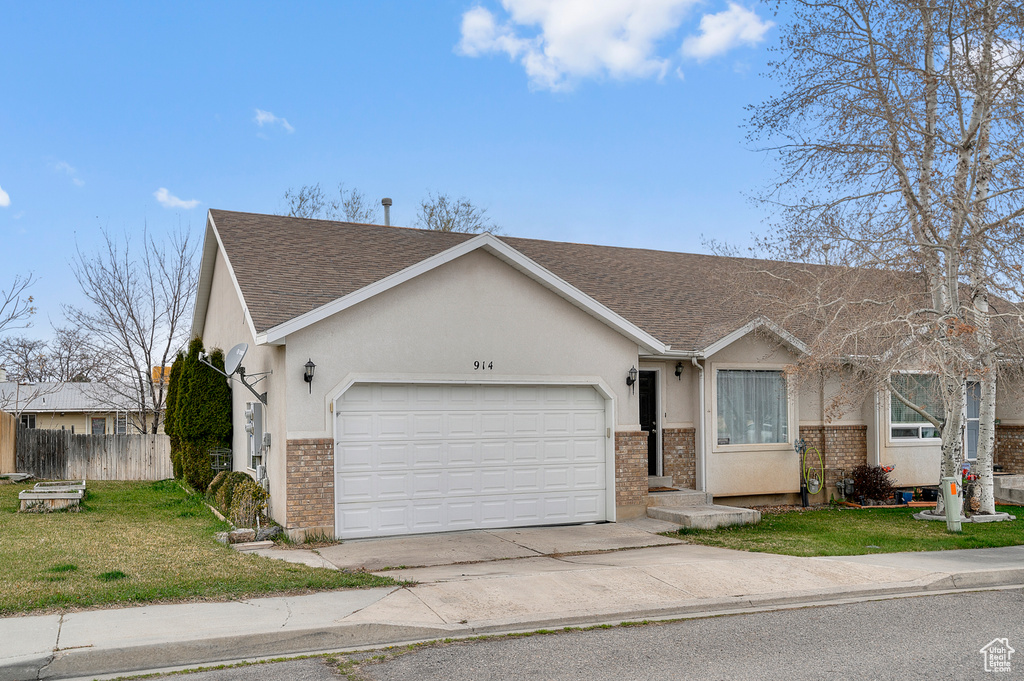 Ranch-style house featuring driveway, a front yard, stucco siding, an attached garage, and fence