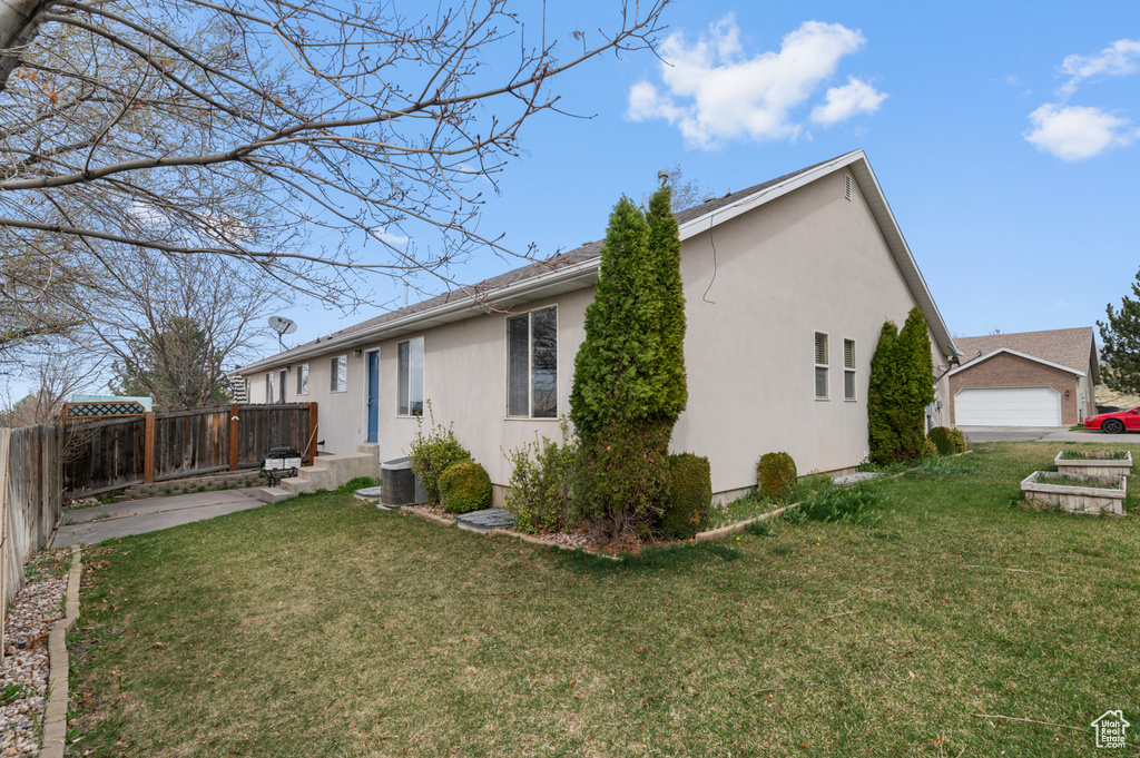 View of side of property with a lawn, fence, and stucco siding