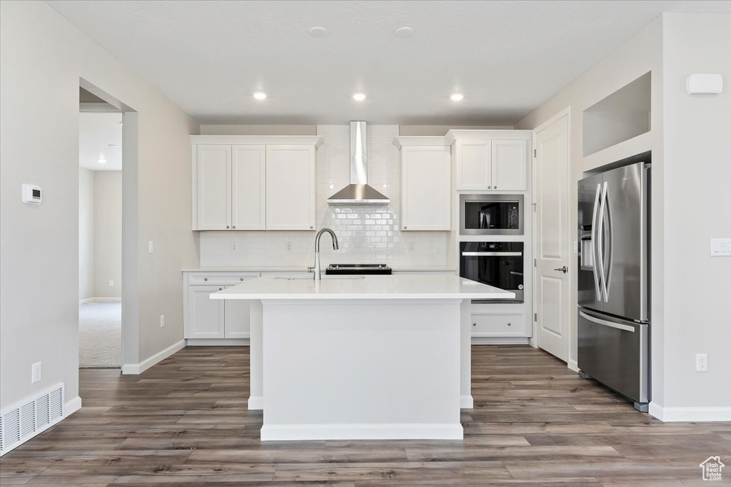 Kitchen featuring decorative backsplash, light countertops, visible vents, appliances with stainless steel finishes, and wall chimney range hood