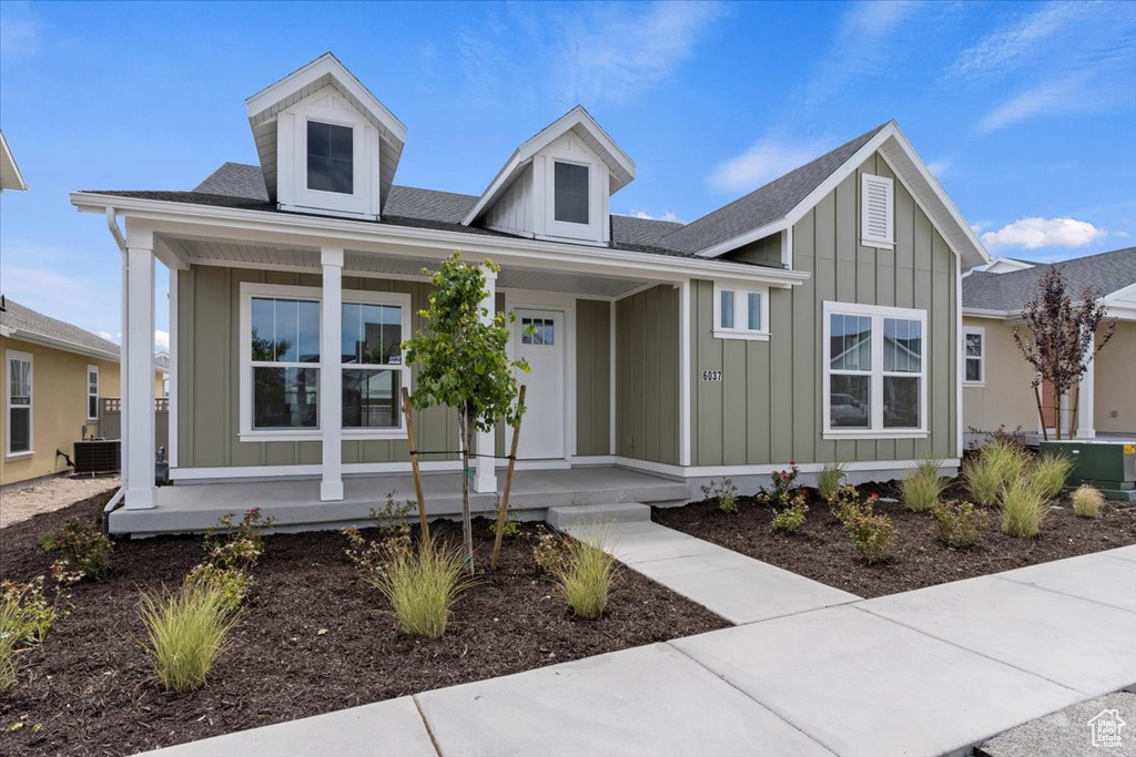 View of front of property with board and batten siding, central AC unit, a porch, and a shingled roof