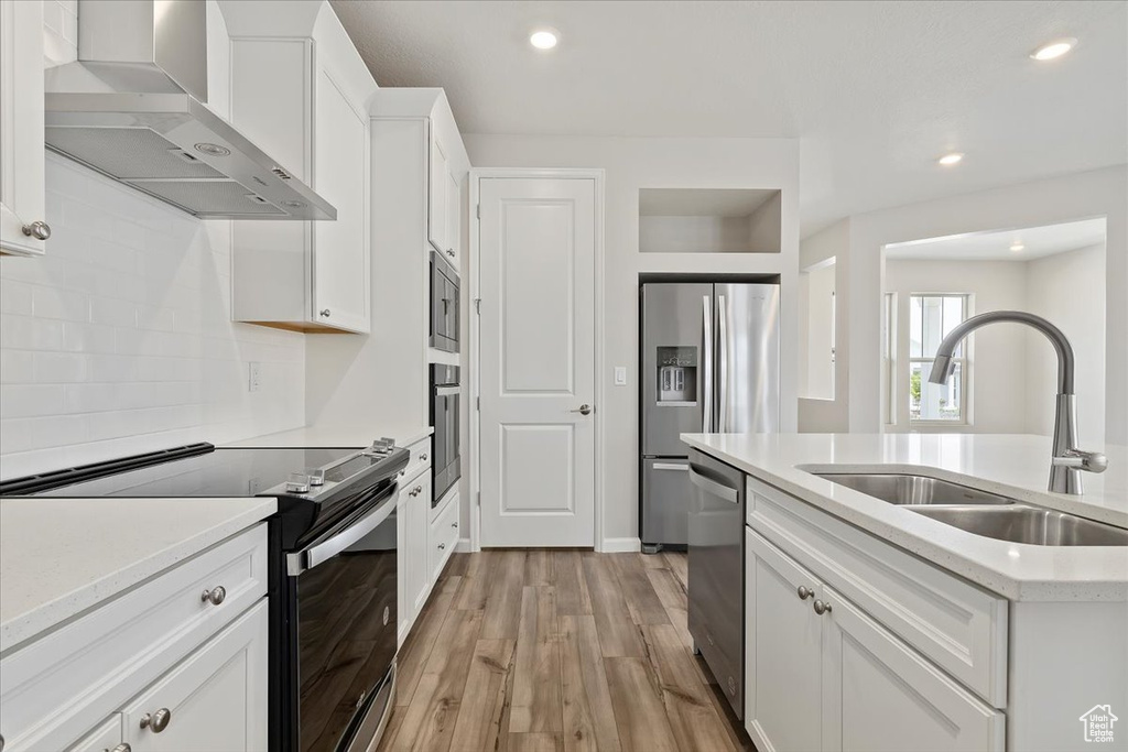 Kitchen with light countertops, a sink, white cabinetry, wall chimney exhaust hood, and stainless steel appliances