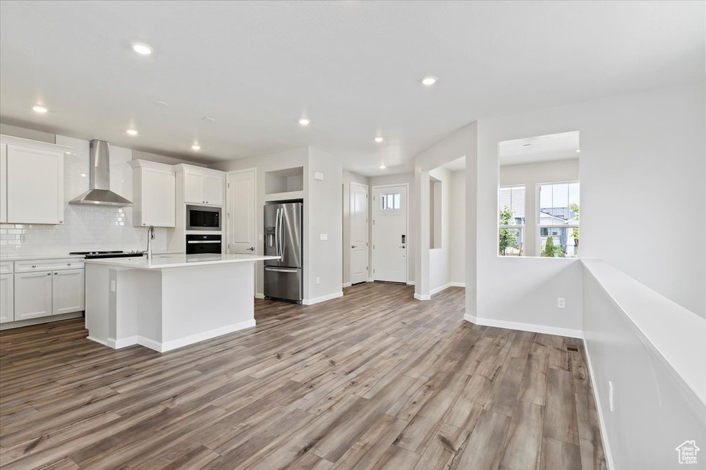 Kitchen with decorative backsplash, white cabinetry, wall chimney range hood, and appliances with stainless steel finishes
