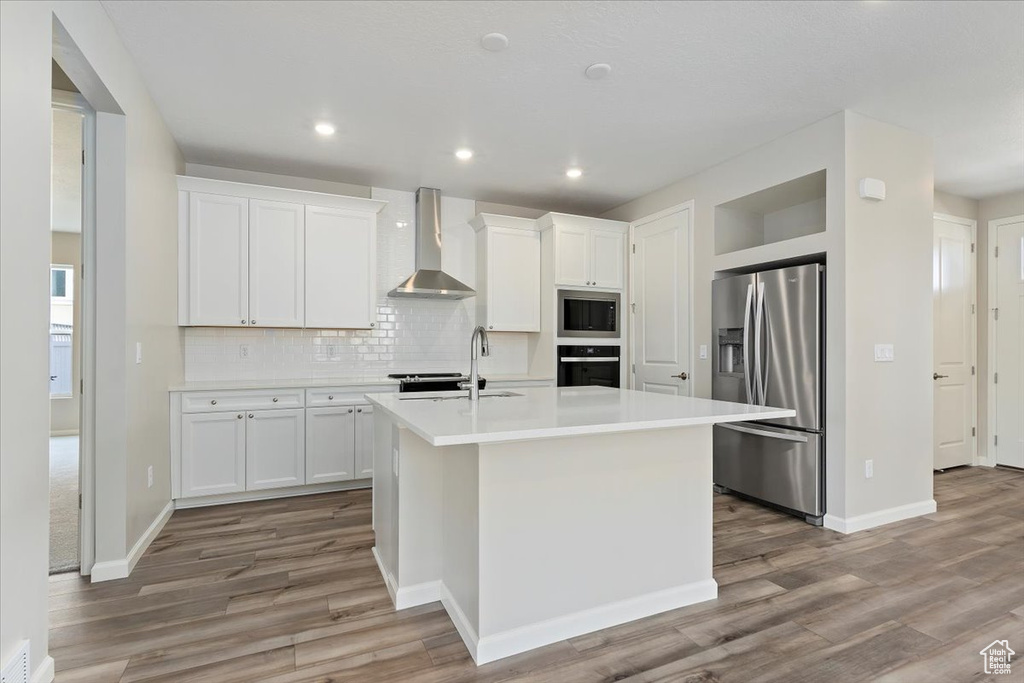 Kitchen with a sink, built in microwave, stainless steel refrigerator with ice dispenser, wall chimney range hood, and oven