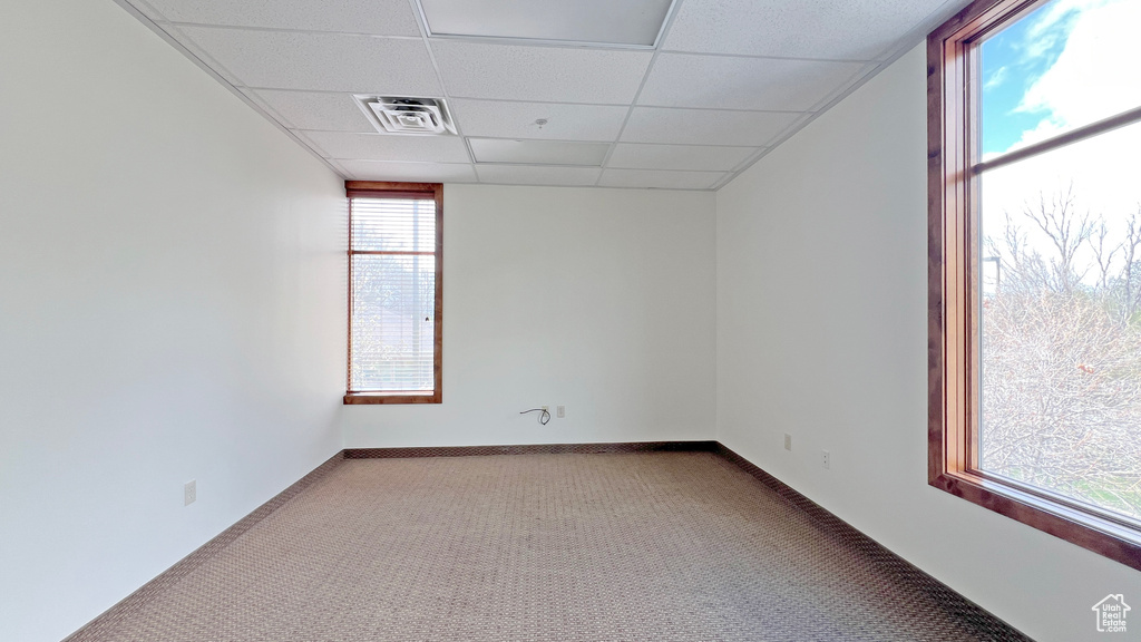 Carpeted spare room featuring baseboards, visible vents, and a drop ceiling