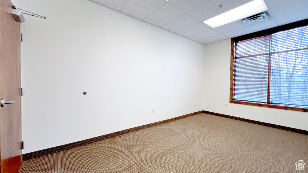 Carpeted empty room featuring baseboards, visible vents, and a drop ceiling